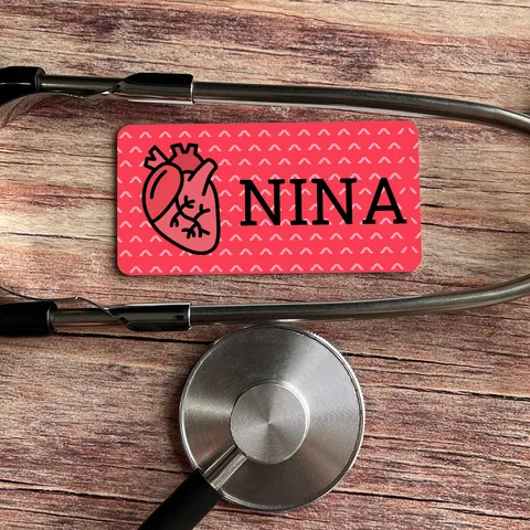 Red heart name badge reading NINA on wood surface next to a silver stethoscope