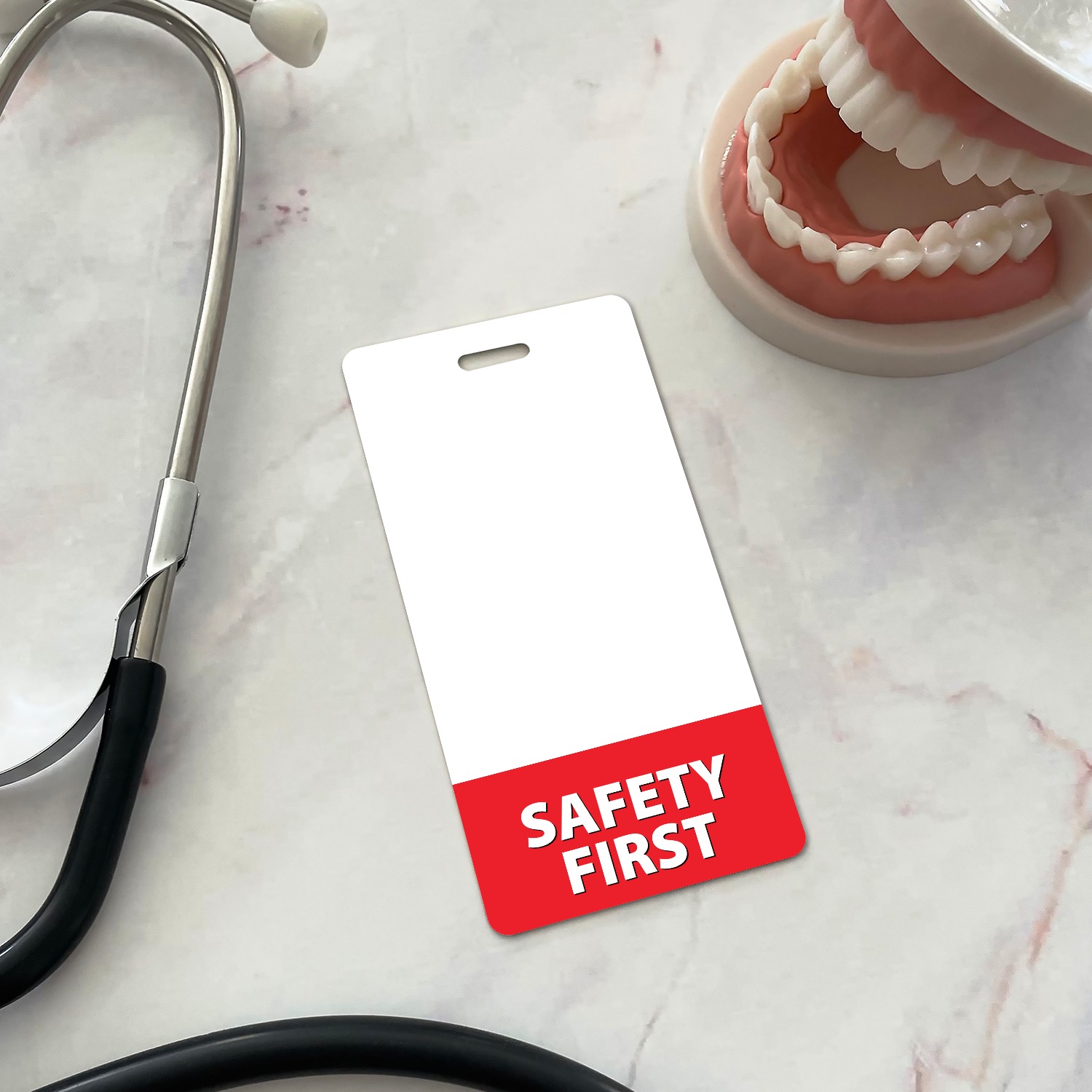 Vertical SAFETY FIRST badge buddy beside a dental teeth model on marble, white with red bottom band