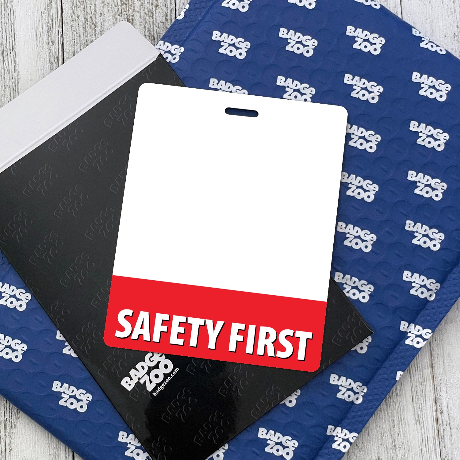 Portrait SAFETY FIRST badge buddy on a blue bubble mailer and black envelope, white top and red band
