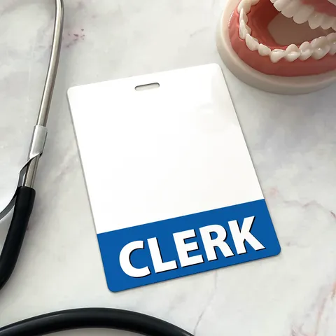 Upright CLERK badge buddy with blue band on marble beside a stethoscope and a dental jaw model