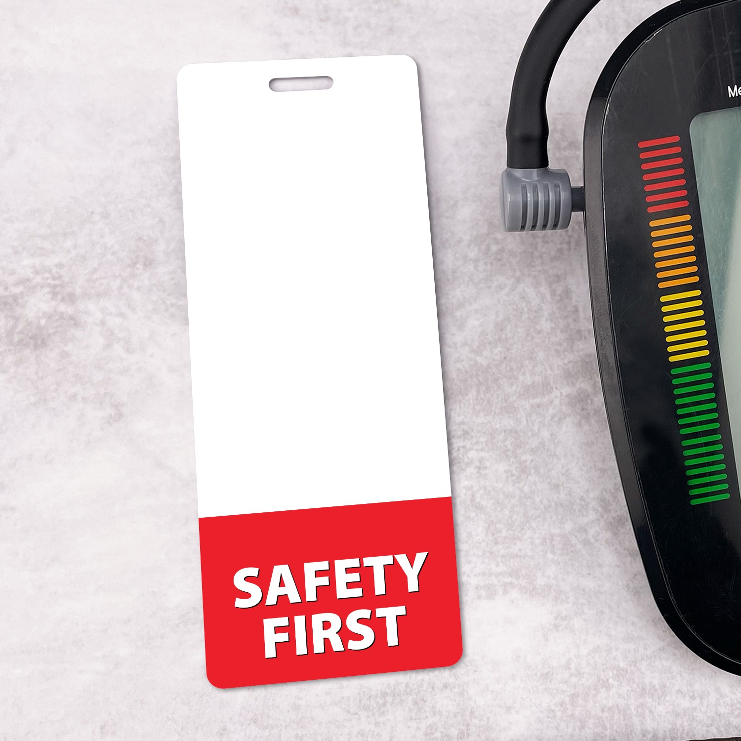 Slim vertical SAFETY FIRST badge buddy next to a blood pressure monitor on light grey surface