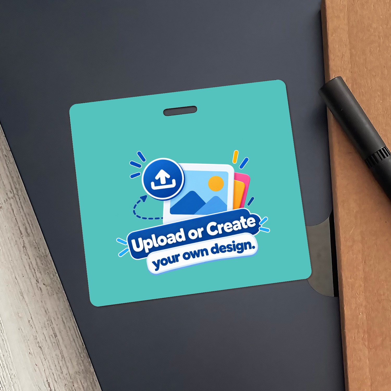 Teal horizontal ID badge with Upload or Create your own design graphic on navy folder next to a black pen
