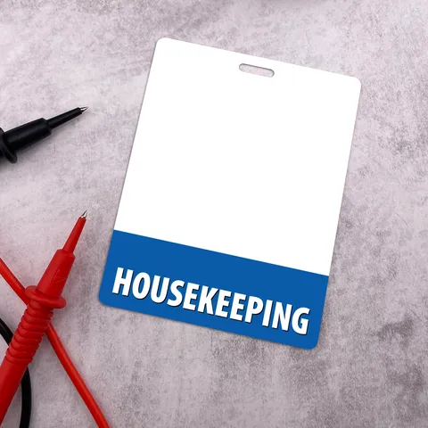 Upright housekeeping badge buddy with blue HOUSEKEEPING band on grey surface beside red and black test probes