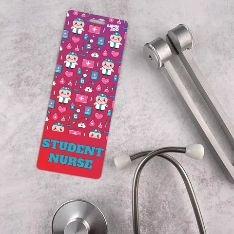 Tall student nurse badge buddy with pink gradient and cartoon nurse pattern, beside a silver stethoscope on grey stone