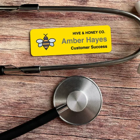Yellow bee name tag reading Amber Hayes beside a silver stethoscope on a wooden table