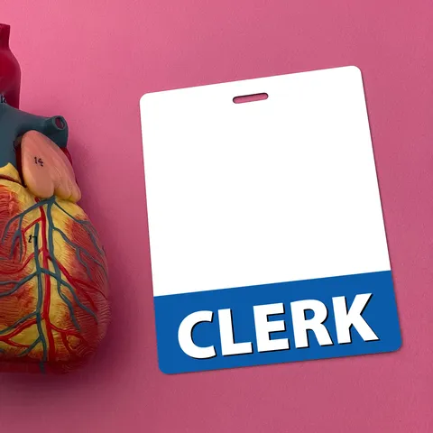 Upright CLERK badge buddy on pink background beside a colorful plastic anatomical heart model
