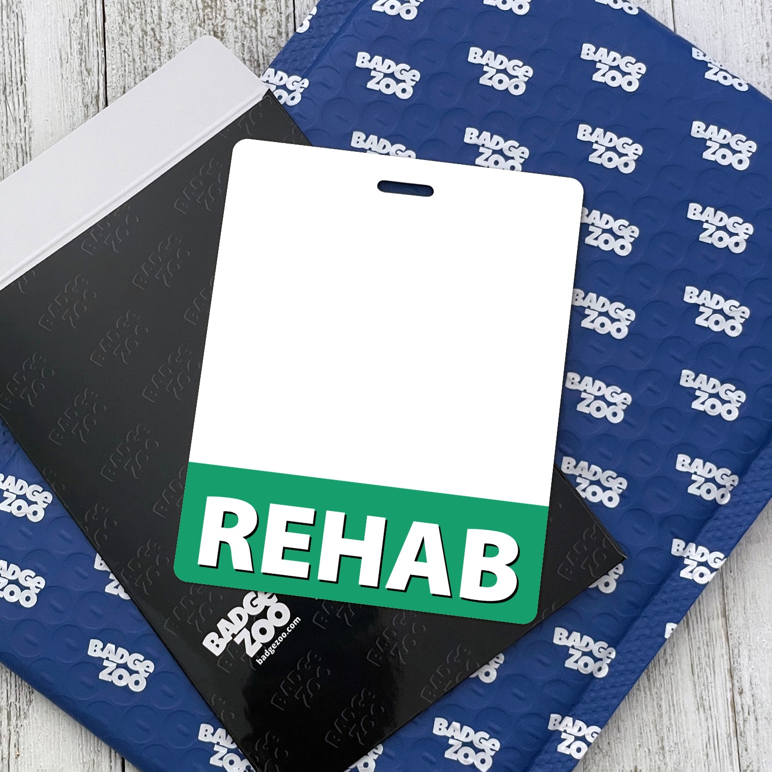 Vertical REHAB badge buddy with green band on blue bubble envelope and black folder with Badge Zoo logo