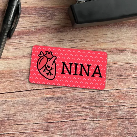 Red name tag with heart graphic and NINA text beside a black pen and stapler on wood