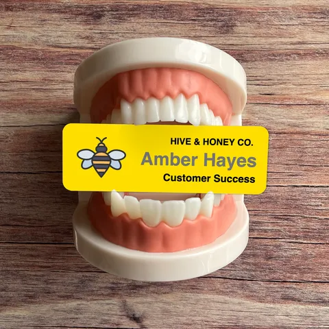 Yellow bee name badge reading Amber Hayes on a set of model teeth on a wooden surface