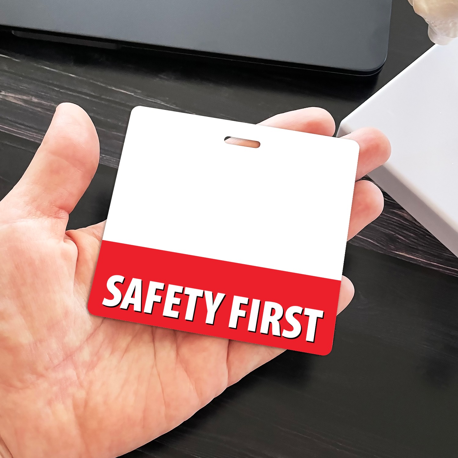 Hand holding a horizontal SAFETY FIRST badge buddy with blank white top and red bottom strip