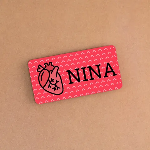 Red name tag with a heart illustration and NINA lettering lying on a tan beige background