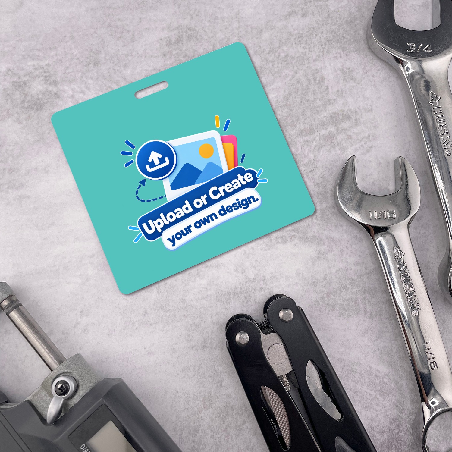 Teal horizontal ID badge with Upload or Create your own design graphic among chrome wrenches and a black multitool