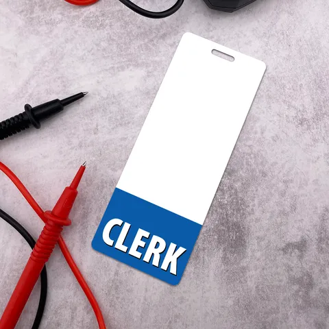 Narrow CLERK badge buddy angled on grey surface beside red and black multimeter probes