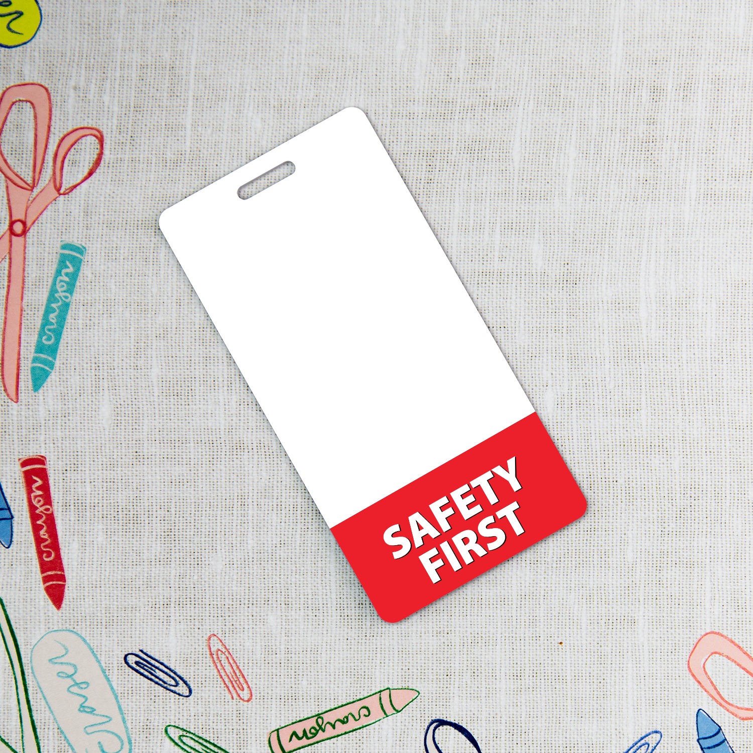 Vertical SAFETY FIRST badge buddy on linen with colorful crayons, scissors and paper clips
