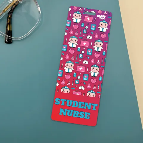 Slim student nurse badge buddy with pink medical icons and teal STUDENT NURSE text, lying on a teal desk