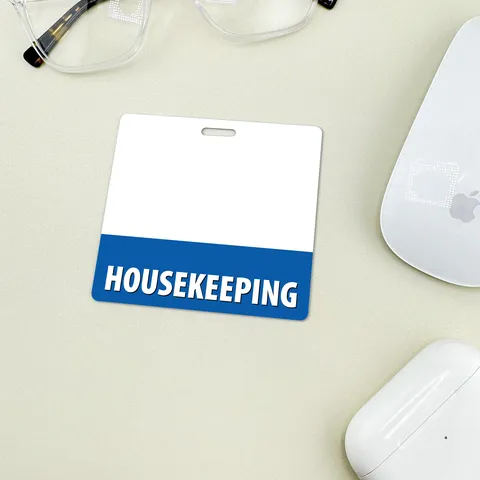White horizontal housekeeping badge buddy with blue HOUSEKEEPING band on desk beside glasses and a white mouse