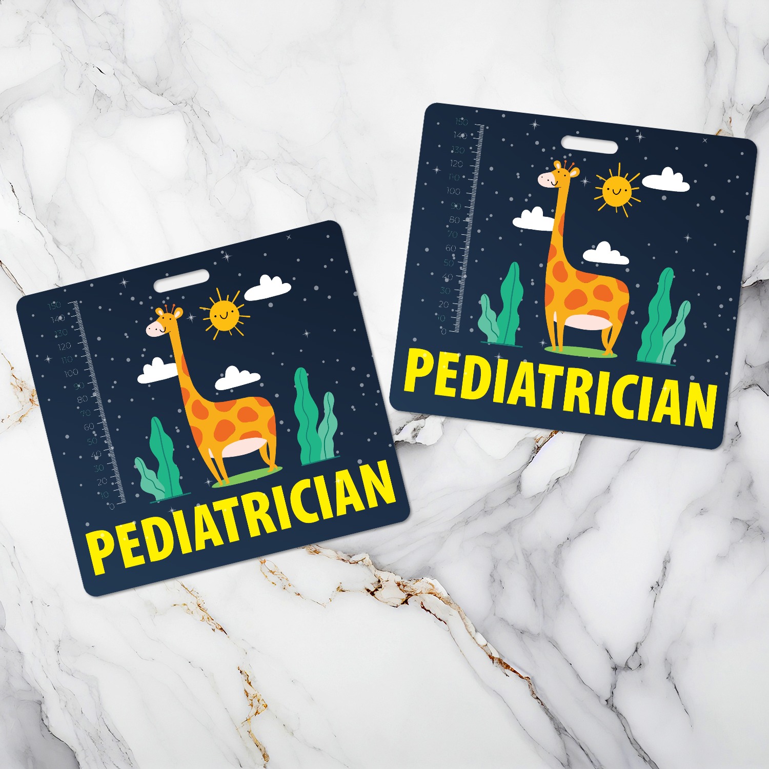 Two pediatrician badge buddies with giraffe night sky design, one angled left and one right, on white marble