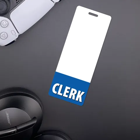 Narrow CLERK badge buddy on dark surface beside a white game controller and black over-ear headphones