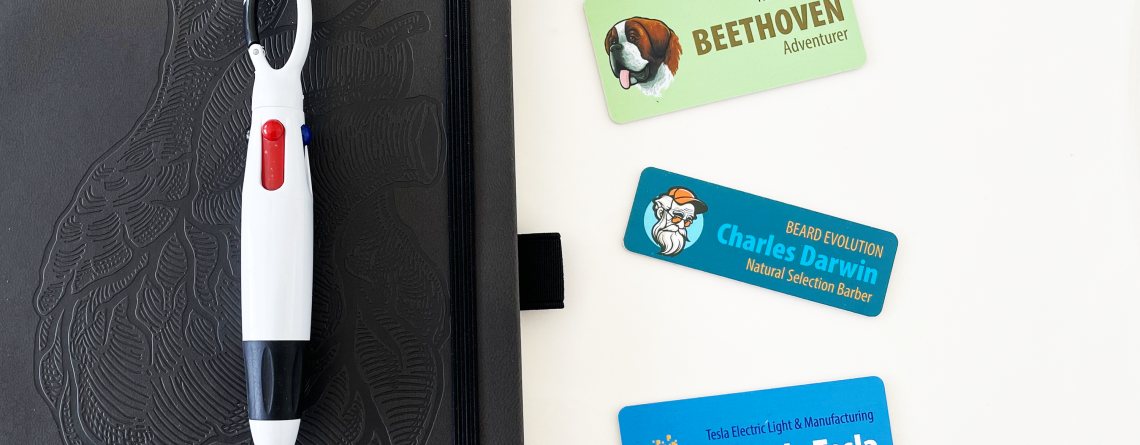 Three custom name tags for pets and professionals next to a black notebook and multi-color pen