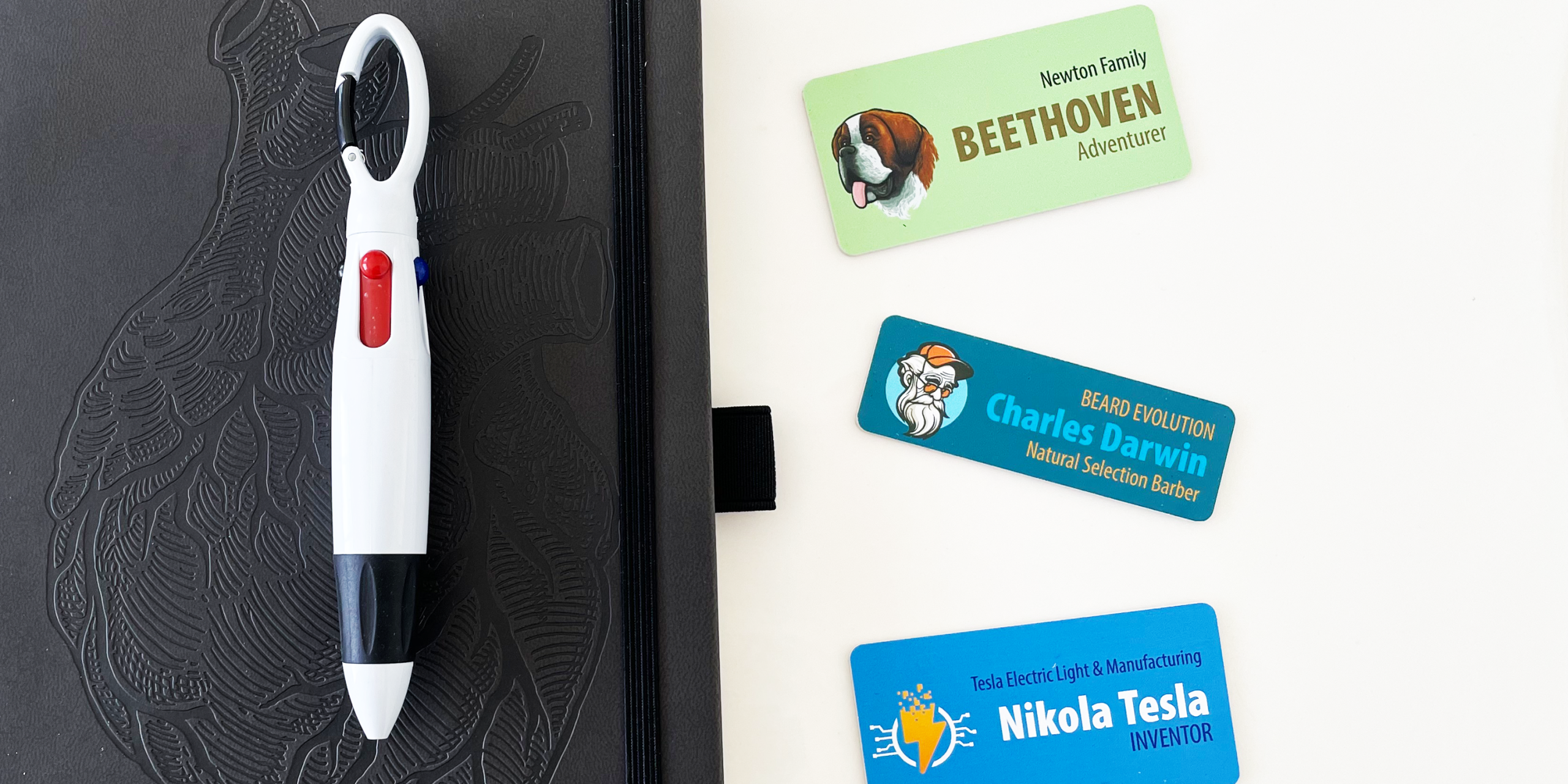 Three custom name tags for pets and professionals next to a black notebook and multi-color pen
