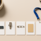 Various name tag backing options including magnet, clip, pin, adhesive, and lanyard, displayed on a neutral background with coffee and notebook.